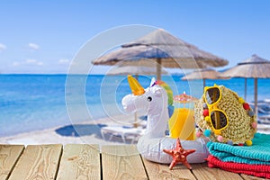 Summer vacation concept with orange juice, beach accessories and unicorn pool float over sea beach background