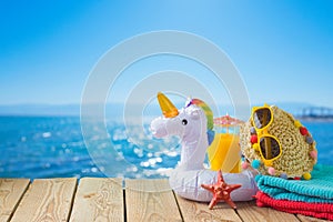Summer vacation concept with orange juice, beach accessories and unicorn pool float over sea beach background