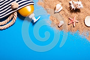 Summer vacation concept with seashells, starfish, women`s beach bag and suntan lotion bottle on a blue background and sand