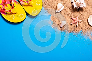 Summer vacation concept with seashells, starfish and women`s beach sandals on a blue background and sand.