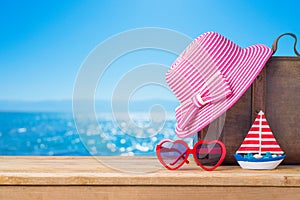 Summer vacation concept with suitcase, sunglasses, hat and boat over sea beach background