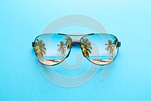 Summer vacation concept. Sunglasses with ocean beach and palms on blue background