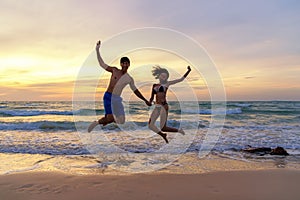 Summer Vacation.  Couple jumping holding hands on tropical on the beach sunset time in holiday trips.  Honeymoon holidays people r photo