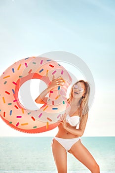 Summer Vacation. Enjoying suntan woman in white bikini with donut mattress near the ocean.