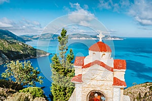 Summer vacation in Greece. Orange colored Hellenic shrine Proskinitari with blue sea and white clouds in background