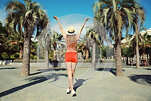 Summer vacation, happy cheerful young woman in full-length raising her hands up on palm tree background