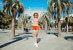 Summer vacation, happy cheerful young woman in full-length raising her hands up on palm tree background