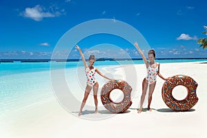 Summer Vacation. Happy free two women with donut float mattress enjoying exotic beach by turquoise water seaside. Maldives island