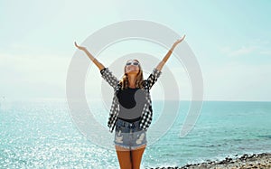 Summer vacation, happy smiling woman raising her hands up on the beach on sea coast background