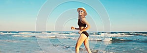 Summer vacation, happy smiling woman walking running in bikini swimsuit and straw hat on the beach on sea coast with waves