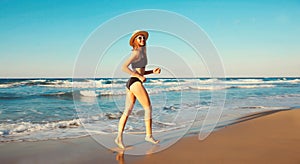 Summer vacation, happy smiling woman walking running in bikini swimsuit and straw hat on the beach on sea coast with waves