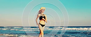 Summer vacation, happy smiling woman walking running in bikini swimsuit and straw hat on the beach on sea coast with waves