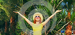 Summer vacation, happy smiling young woman raising her hands up on the beach on palm tree background