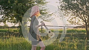 Summer vacation, happy teenage girl walking on country road with ukulele guitar, fashionable hipster with dyed hair