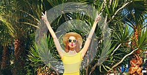 Summer vacation, happy young woman raising her hands up wearing straw hat, shorts on the beach on palm tree background