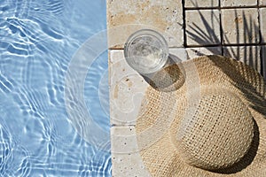 Summer vacation. Hat on the travertine stone by the beautiful swimming pool. Blue sea surface with waves, texture water.