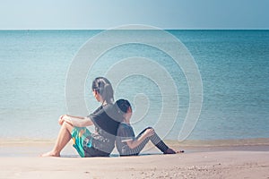 Summer Vacation and Holiday Concept : Happy family day trip at the sea, Woman and child sitting back to back relax on sand beach.