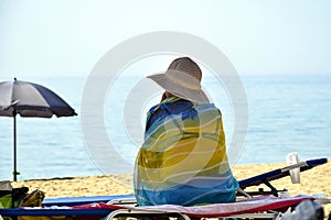 Summer vacation holidays. Beach relaxation. Elderly woman sits on chaise-longue under an umbrella on beach