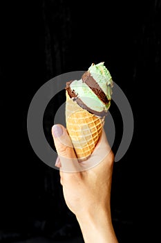 Summer, vacation, ice cream. The hand holds soft ice cream in a chocolate-mint waffle cup. On a black background, close-up