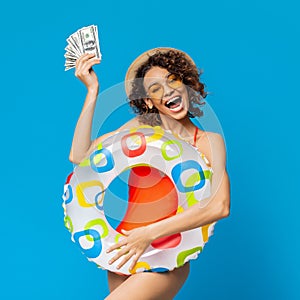 Summer Vacation. Joyful black girl holding bunch of money and inflatable ring