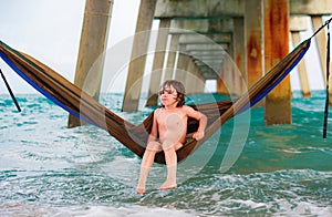 Summer vacation, kid boy in colorful hammock in sea.