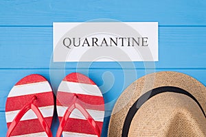 Summer vacation and quarantine concept. Top above overhead view photo of word quarantine flipflops and hat isolated on blue wooden