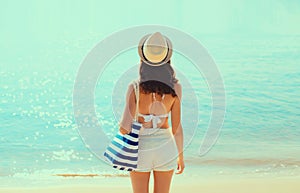 Summer vacation, rear view of beautiful young woman with bag in bikini swimsuit and straw hat on the beach on sea coast background