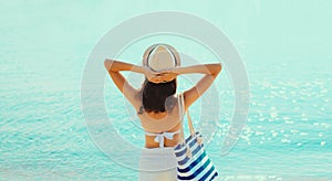 Summer vacation, rear view of beautiful young woman with bag in bikini swimsuit and straw hat on the beach on sea coast background