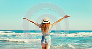 Summer vacation, rear view of happy woman raising her hands up on the beach on sunny day on sea background