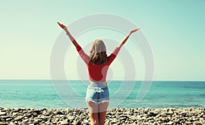 Summer vacation, rear view of happy woman raising her hands up on the beach on sunny day on sea background