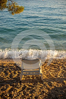 Summer vacation scene. A white beach deck chair in a golden hour sunset on beautiful Adriatic coast in Croatia with crystal clear