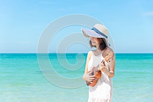 Summer Vacation. Smelling asian women relaxing and playing an ukulele on the beach, so happy and luxury in holiday summer, blue sk
