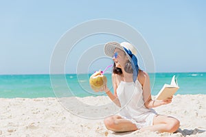 Summer Vacation. Smelling asian women relaxing, reading book and drinking coconut cocktail on the beach,