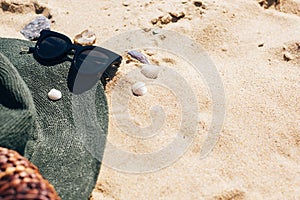 Summer Vacation. Stylish hat, sunglasses and straw bag on sandy beach with sea shells. Girl accessory on the beach. Hello summer