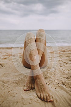 Summer vacation. Tanned legs of a girl on beach with sand on smooth skin. Beautiful authentic and unusual image. Young woman