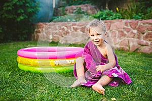 Summer vacation theme. A small 3 year old Caucasian boy playing in the backyard of a house on the grass near a round inflatable co