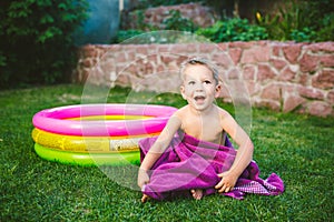 Summer vacation theme. A small 3 year old Caucasian boy playing in the backyard of a house on the grass near a round inflatable co