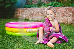 Summer vacation theme. A small 3 year old Caucasian boy playing in the backyard of a house on the grass near a round inflatable co