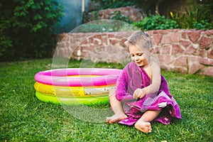 Summer vacation theme. A small 3 year old Caucasian boy playing in the backyard of a house on the grass near a round inflatable co