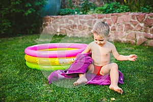 Summer vacation theme. A small 3 year old Caucasian boy playing in the backyard of a house on the grass near a round inflatable co