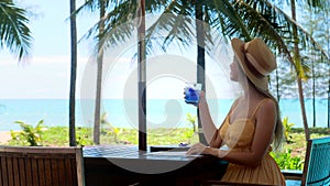 Summer vacation in tropical resort. Woman sitting in beachside cafe and drinking refreshment iced drink, enjoy sea and