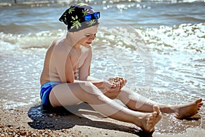 Summer and Vacations concept. Teenager boy holds many sea shells in his hands in swimming trunks and a bandana with blue glasses