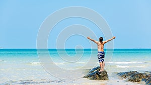 Summer vacations. Lifestyle man raise arm relax and chill on the rock, blue beach and sky background.