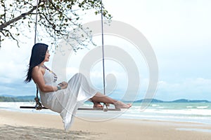 Summer Vacations. Lifestyle women relaxing and enjoying swing on the sand beach, fashion stunning women with white dress on the tr