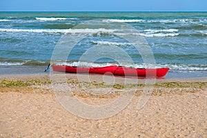 Summer Vacations. The red kayak is parked on the sandy beach on a sunny day, waiting for people to paddle out to sea.