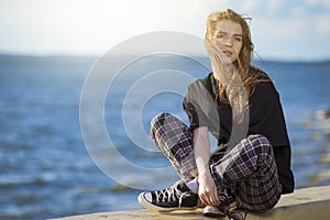 Summer Vacations.  Relaxing Caucasian Blond Female Girl in Street Clothing Posing Outdoors While Sitted On Fence Outdoors At Sunny