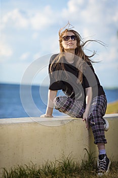 Summer Vacations.  Relaxing Caucasian Blond Female Girl in Street Clothing Posing Outdoors While Sitted On Shoreline Outdoors At