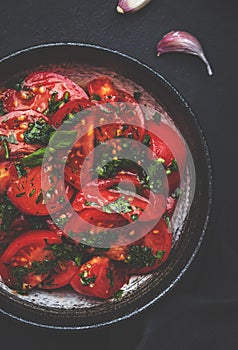 Summer vegan tomato salad with parsley, garlic, pepper and olive oil dressing, black table background, top view