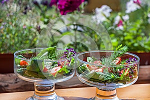 Summer vegetables salad with fresh strawberries, basil, mozzarella and edible flowers in glass salad-bowls in garden at sunny day