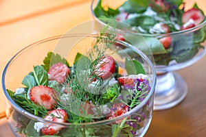 Summer vegetables salad with fresh strawberries, basil, mozzarella and edible flowers in glass salad-bowls in garden at sunny day